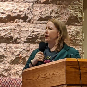 A close-up of Tessa standing at a podium and talking into a microphone.